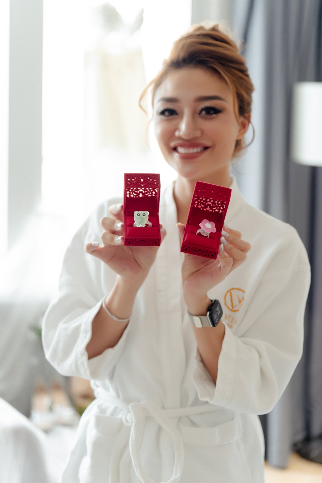 Cô dâu khoác áo choàng trắng tươi cười khoe cặp nhẫn cưới trong hộp đỏ